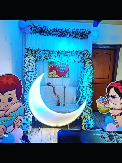 A simple and sweet baby shower decoration for home. The setup includes a lighted moon, a floral swing, and cute baby cutouts.