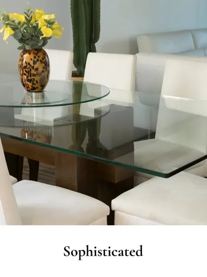 A sophisticated dining experience defined by a glass-top table, plush white chairs, and a simple floral centerpiece, creating a clean and modern aesthetic.