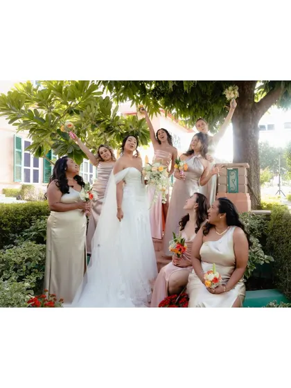 A fun and joyful moment between the bride and her bridesmaids, all laughing and celebrating together in a garden setting.