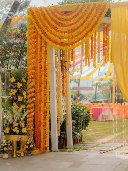 A beautiful entrance archway for a Haldi ceremony, heavily decorated with garlands of yellow and orange marigolds. This traditional floral decor provides a vibrant welcome for guests.