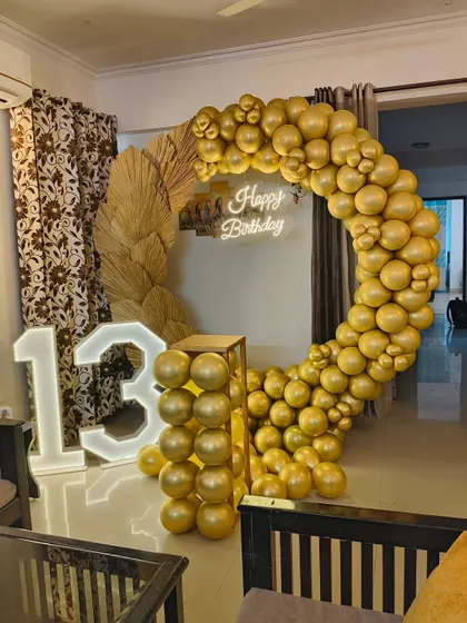 A luxurious all-gold balloon ring for a 13th birthday. This striking design is paired with dried pampas grass details, a neon sign, and a light-up number '13'.