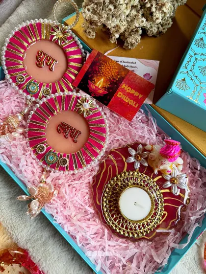 A pink and red Diwali hamper with "Shubh Labh" hangings and a Ganesha-themed diya.