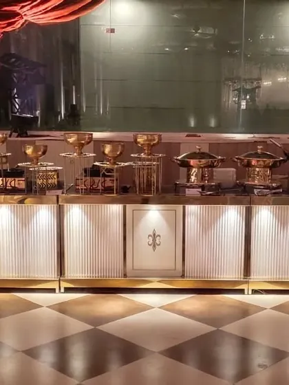 A clean and sophisticated buffet setup with white and gold counters against a checkered floor, ready to serve a variety of delicious hot dishes.