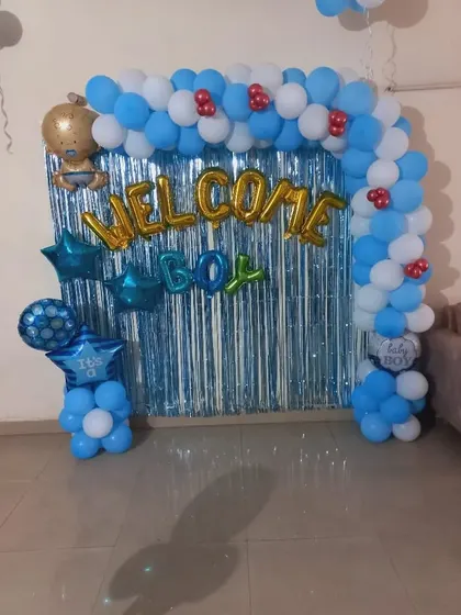 A 'Welcome Boy' balloon arch with a blue fringe curtain. The arch is decorated with star and baby-themed foil balloons.