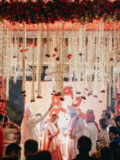 The couple participates in a ritual during their pheras, surrounded by guests under a canopy of hanging floral strings, capturing the sacred and communal feeling of the ceremony.