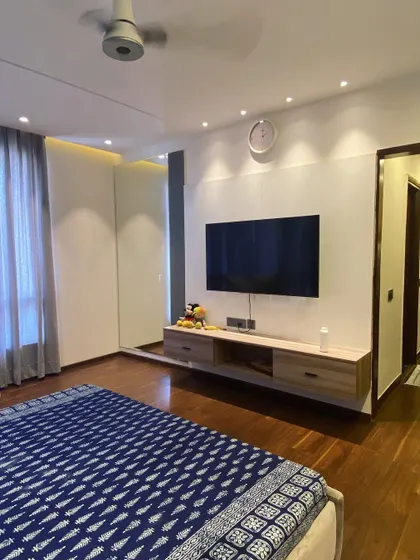 This master bedroom in Noida features a floating TV unit and warm wooden flooring. The design is clean and minimalist, creating a spacious and relaxing atmosphere.