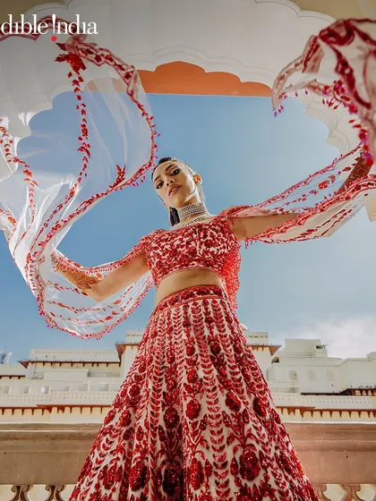 A bride shows off her flowing red and white dupatta against the backdrop of a Jaipur palace.