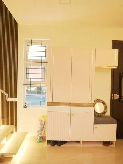 An entryway featuring an illuminated staircase, a sleek shoe rack with a seating nook, and vertical wooden louvers for a modern and welcoming first impression.