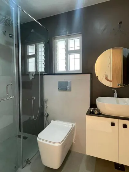 An on-site photo of a newly completed modern bathroom. It features dark textured walls, a wall-mounted toilet, a glass shower partition, and a simple vanity with a vessel sink, showcasing a clean and contemporary design.