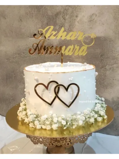 Simple elegance for an engagement celebration. This cake is decorated with delicate baby's breath, interlocking hearts, and a custom gold topper with the couple's names.