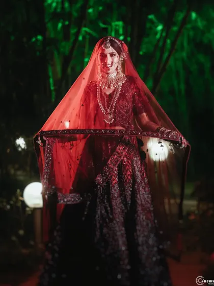 A dramatic nighttime portrait of a bride holding her veil. The red light and dark background create a bold and captivating image.