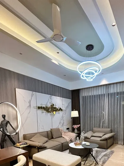 A luxurious living room featuring a complex, multi-layered false ceiling design with integrated lighting. This architectural detail becomes a major focal point of the room.