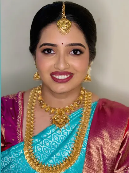 A classic South Indian bridal portrait for Navya's Muhurtham. Her makeup features defined eyes and a rich berry lip color, complementing her vibrant saree.