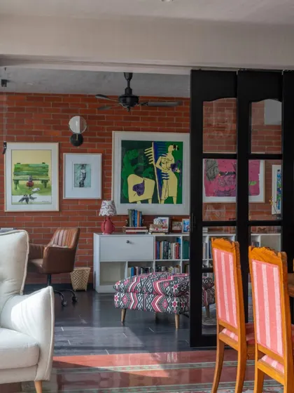 A view into the study of the Dhaka home, where a wall of exposed brick is layered with colorful art. The space is designed to be inspiring and personal, a place where work and creativity can flourish.