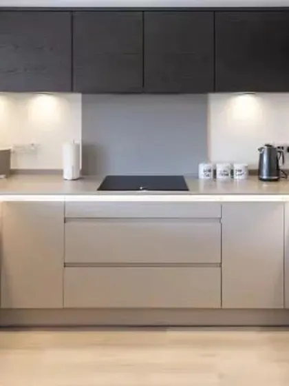 A minimalist U-shaped kitchen with handleless cabinets and integrated LED strip lighting. The two-tone effect with dark upper cabinets adds depth to the design.
