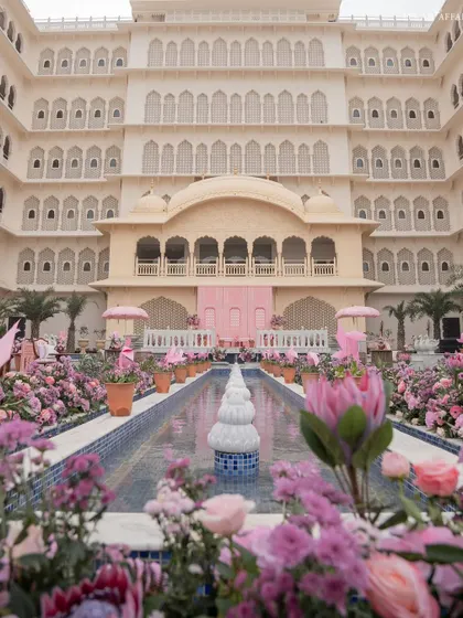The stunning view of the Mehendi setup at Anantara Jaipur, with a long water body lined with pink florals leading towards the palace-like venue.