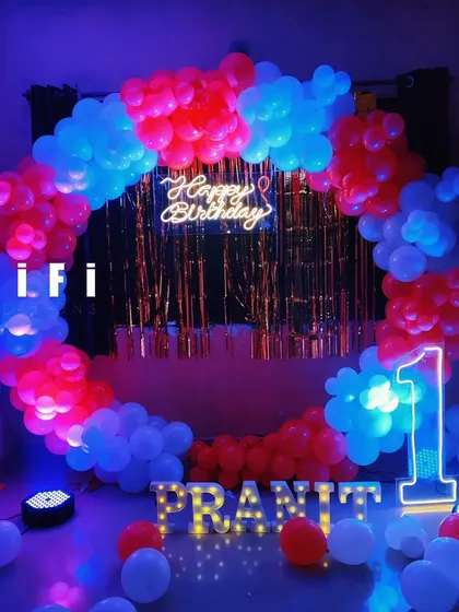 A vibrant and bold ring backdrop for a first birthday. The striking combination of red and blue balloons, a gold tinsel curtain, and glowing neon and marquee lights makes for an energetic and exciting party decoration.