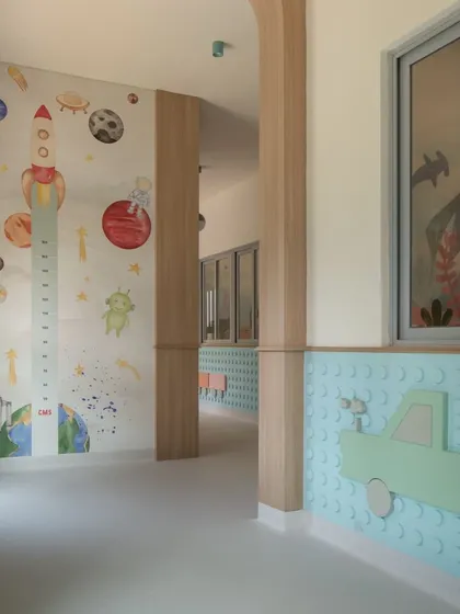A corridor in the nursery section featuring a space-themed height chart and a tactile, lego-inspired wall panel. This multi-sensory design encourages interaction and keeps the walls clean from hand marks.