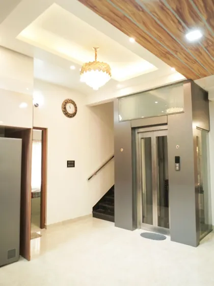 A luxurious entryway in a villa, featuring a private elevator, a wooden textured false ceiling, and elegant lighting fixtures.