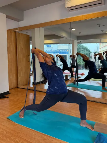 A student uses a strap to deepen a lunge and open her shoulders, showing how props can enhance a stretch.