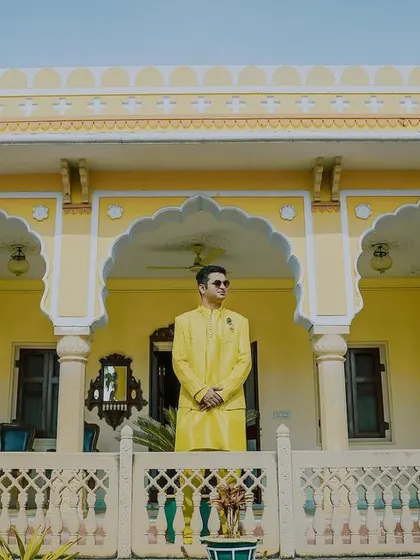 A groom looking regal on the balcony of a palace during the haldi ceremony. His bright yellow kurta stands out against the matching yellow architecture, creating a striking portrait.