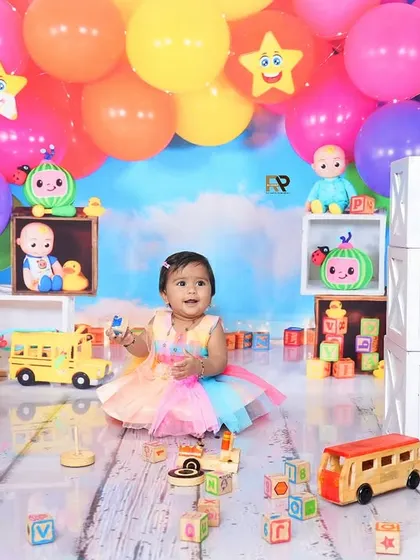 A baby girl sits among a colorful array of Cocomelon toys and balloons. This theme is perfect for capturing the joy and excitement of a first birthday.