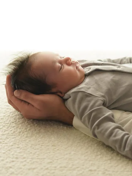 A parent's hand gently supports their newborn's head. This shot beautifully illustrates the scale of how small they are, and how much they are loved.