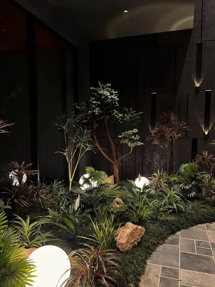A nighttime view of the indoor garden, where uplighting on the dark wall panels adds another layer of dimension. The entire scene is designed to be a captivating visual experience.
