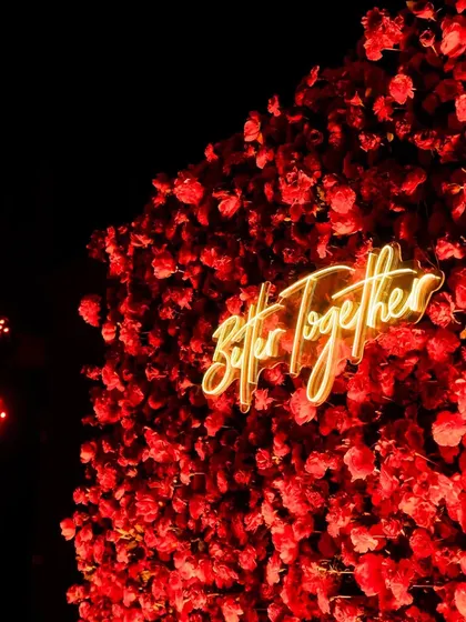 A close-up of a massive wall of red roses with a "Better Together" neon sign, creating a bold and romantic focal point for a Sangeet night.