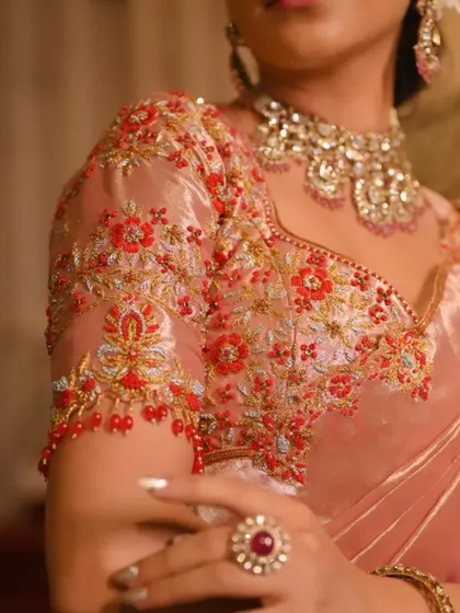 A detailed shot of a hand-embroidered blouse sleeve in a beautiful peach-pink tissue silk, adorned with red and gold threadwork.
