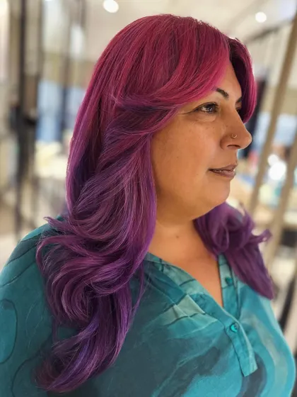A fun and vibrant look with curtain bangs and face-framing layers. The pink and violet hair color makes a bold statement, and the cut adds beautiful shape.
