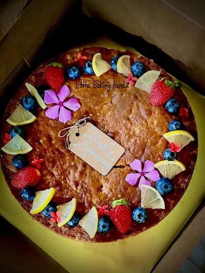 A top view of the tangy lime cake with mixed berries, decorated with fresh flowers and a custom tag for an anniversary celebration.
