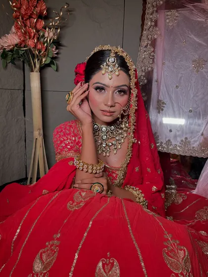 A seated portrait of the bride, showcasing the rich embroidery of her red lehenga and the flawless application of her makeup.