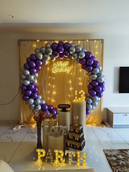 A full shot of the blue and purple themed birthday decor. The fairy light backdrop adds a warm glow behind the balloon ring, creating a great photo opportunity for the birthday boy.