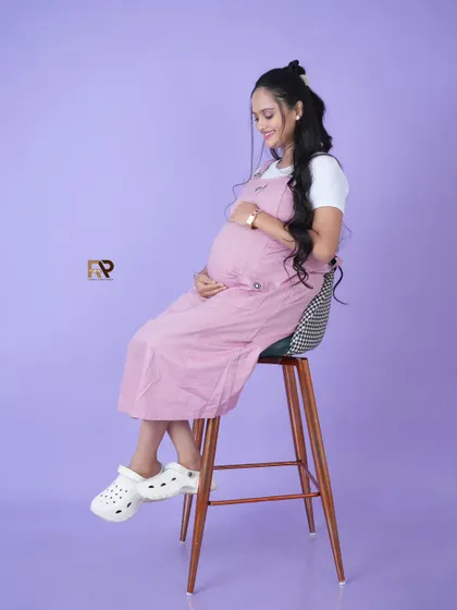 A casual and cute look. The mom-to-be wears a pink dungaree dress over a white t-shirt, perfect for a relaxed and playful modern maternity shoot.