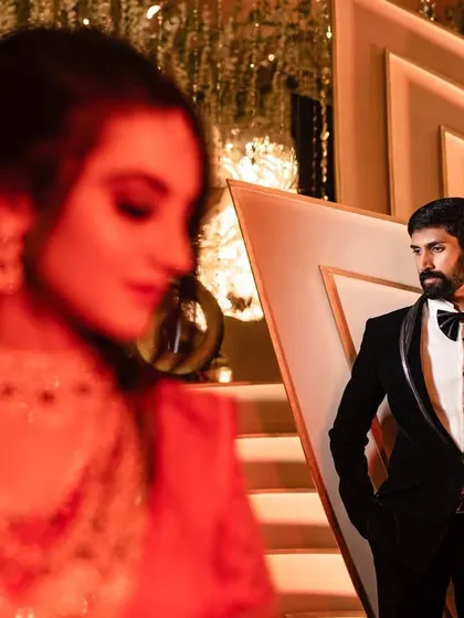 An artistic shot focusing on the groom in his sharp tuxedo, with the bride softly blurred in the foreground. This creative composition tells a story of anticipation.