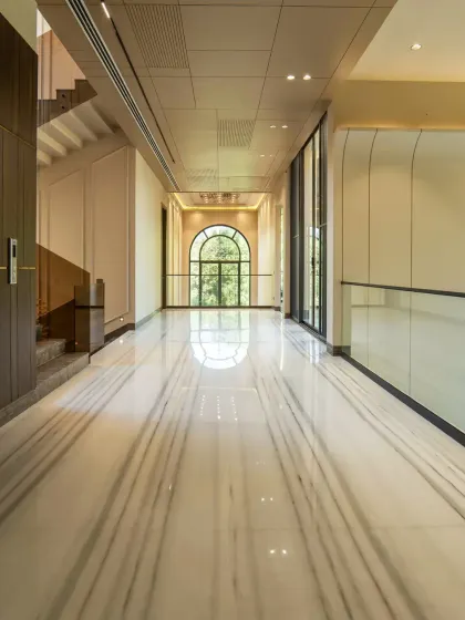 A long corridor in the Sultanpur farmhouse, showcasing the reflective Equator White marble flooring with William Grey accents. The design uses clean lines and a grand archway at the end to draw the eye and create a sense of scale.