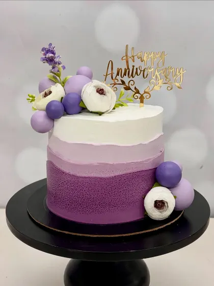 This anniversary cake features a stunning purple ombre design, decorated with purple spheres and delicate white and purple flowers. It's a cake that shows up dressed better than you!