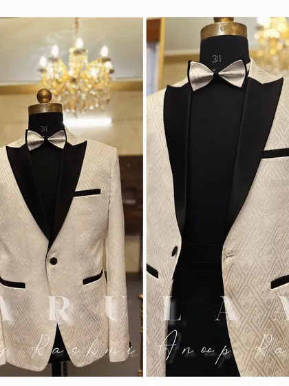 A classic white tuxedo jacket with a modern twist. This piece features a textured geometric pattern on the fabric, contrasted with sharp, solid black satin lapels and pocket details for a timeless black-tie look.