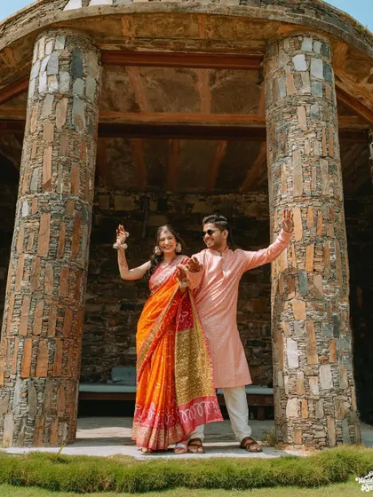 A fun, posed shot of the couple striking a dance pose within a stone gazebo at their Udaipur wedding venue.