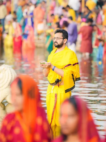 A man in traditional yellow attire offers prayers in the water during Chhath Puja. The festival is observed by both men and women with equal devotion.