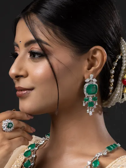 A close-up profile shot focusing on the intricate details of the emerald earrings and maang tikka from the bridal set.