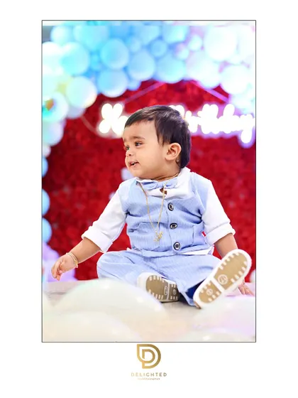A happy moment from a little boy's first birthday party. The colorful balloon arch and his joyful expression create a timeless memory.