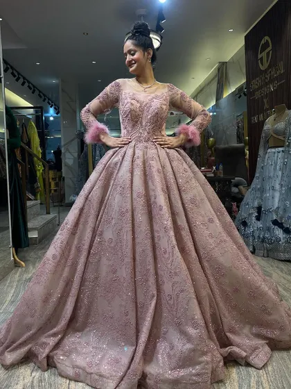 A full view of our glittery dusty pink Cinderella ball gown. The long sleeves with feather cuffs, fitted bodice, and voluminous skirt create a balanced and elegant silhouette. It’s a perfect choice for a winter engagement or reception.