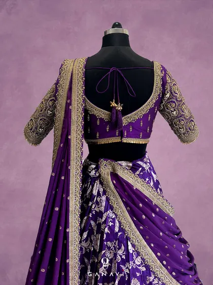 The back of this purple lehenga blouse features an elegant deep-cut design, intricate border embroidery, and beautiful tassels, ensuring you look stunning from every angle.