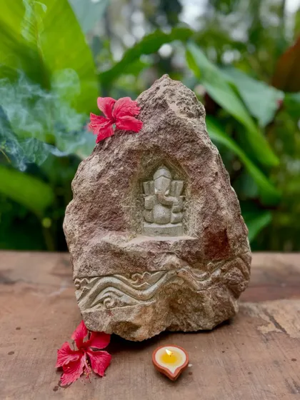 A Ganesha carving in a natural rock niche, with incense smoke adding to the serene atmosphere. The artist chisels the form with utmost care, creating a unique piece that blends rustic charm with divine art.