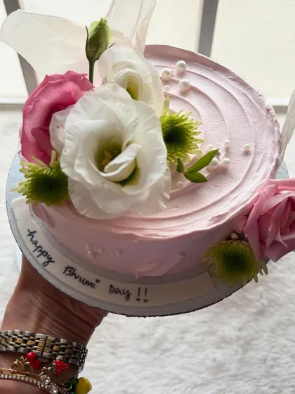 Holding up this beautiful floral cake, decorated with fresh pink and white roses. It's perfect for any celebration that needs a touch of elegance.