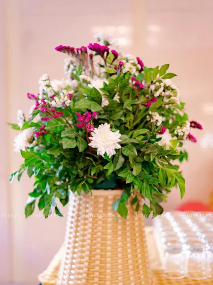 This floral arrangement in a woven wicker basket adds a touch of rustic charm to the decor. The mix of white chrysanthemums, purple statice, and fresh greenery is perfect for a daytime event with a natural aesthetic.