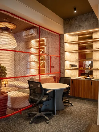 A semi-private discussion nook, defined by a red mesh partition. This space combines a formal meeting table with a more relaxed lounge area in the background.