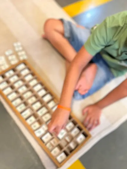 Working with the movable alphabet, this child is exploring the building blocks of language. This tactile approach to spelling and reading allows children to compose words and sentences long before they can write them by hand.